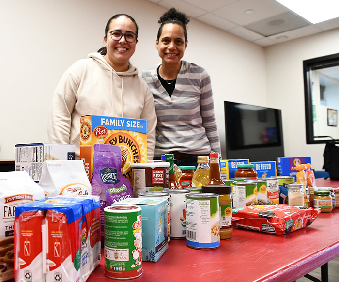 two women standing behind a table with donated food items
