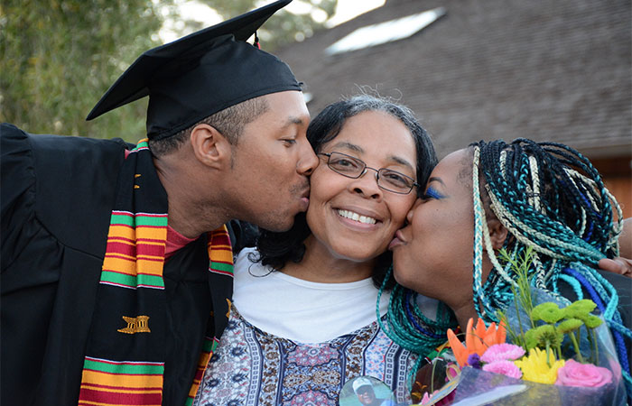 two graduates kissing a woman