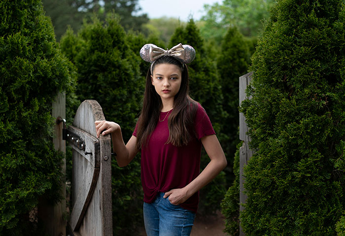 Young girl with micky mouse ears in front of fence