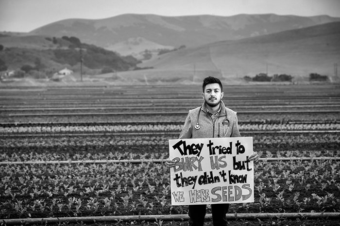 male standing in field with mountain backdrop holding sign